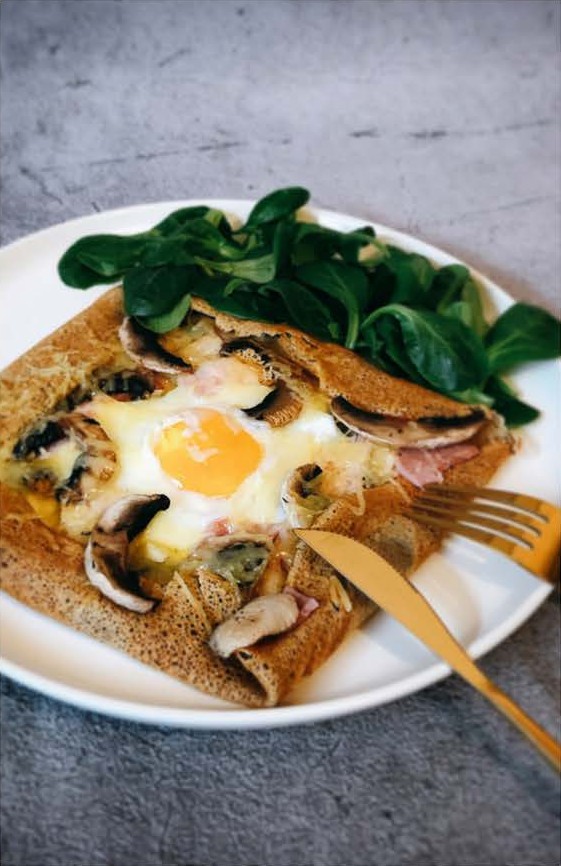 Galette de sarrasin garnie d'un œuf, de champignons et de jambon, servie avec de la mâche